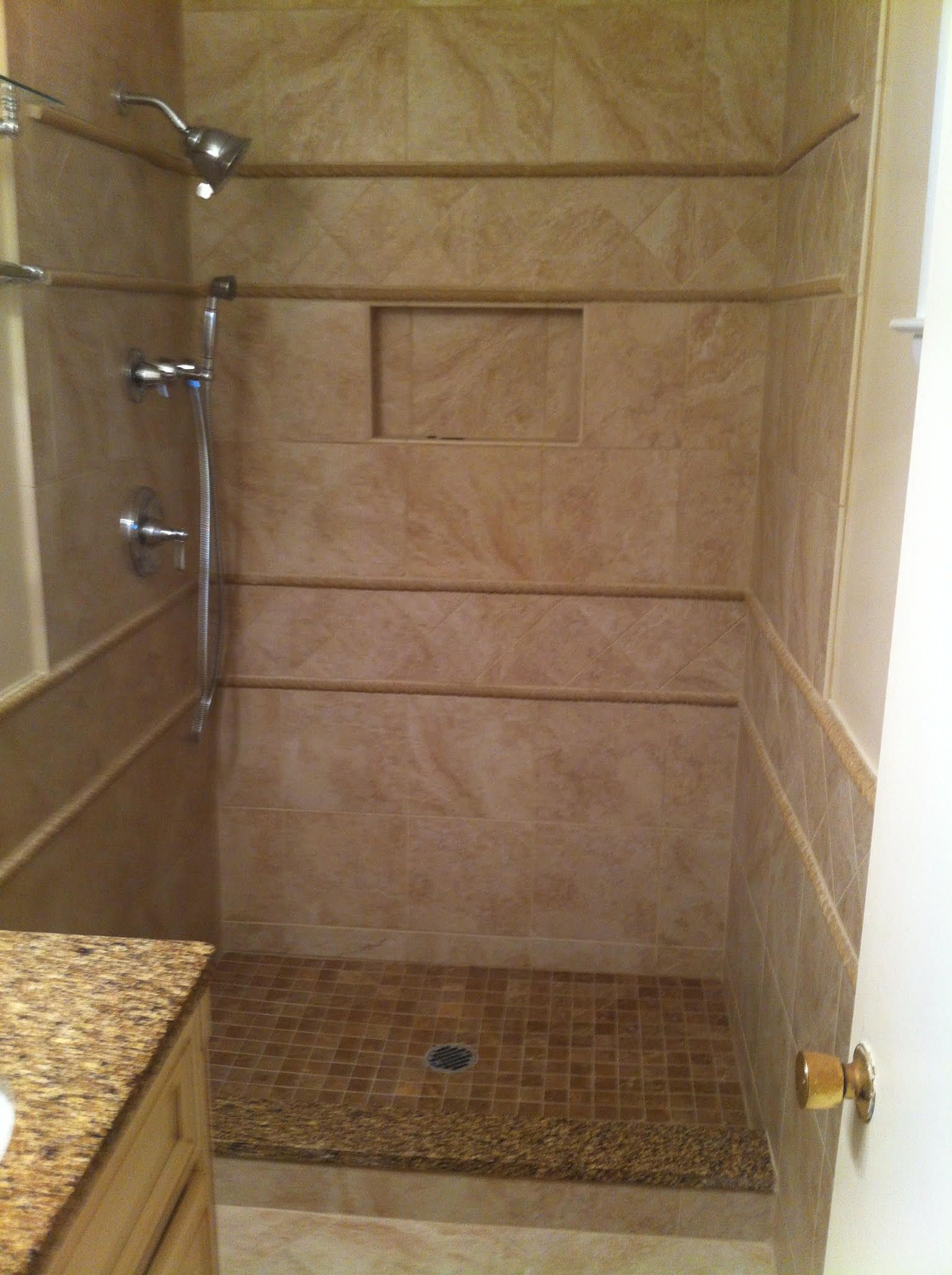 Shower stall with light brown tiles, mosaic floor, and built-in shelf.