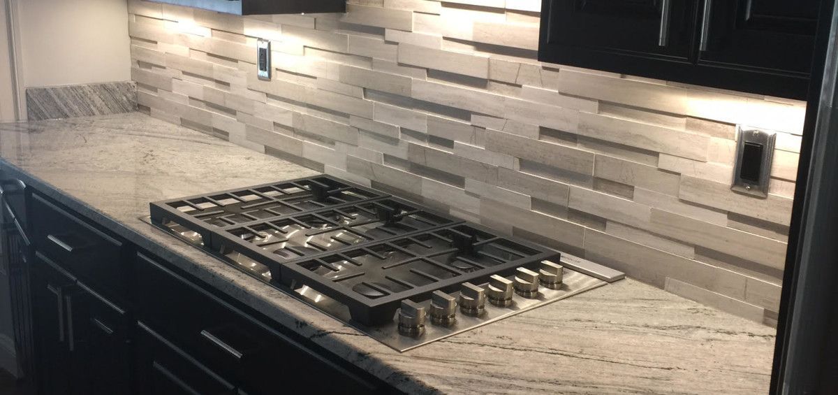 Kitchen counter with gas cooktop, gray granite, and backsplash with under-cabinet lighting.