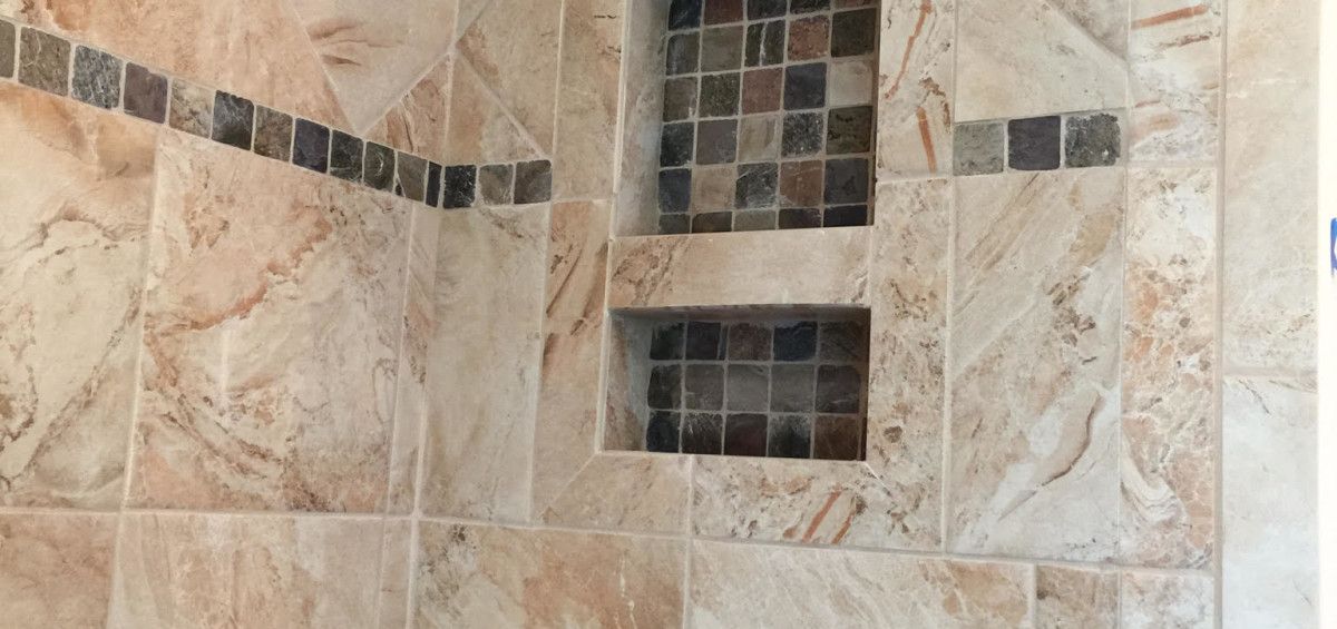 Tiled shower with inset shelves, featuring neutral stone-like tiles and mosaic accents.