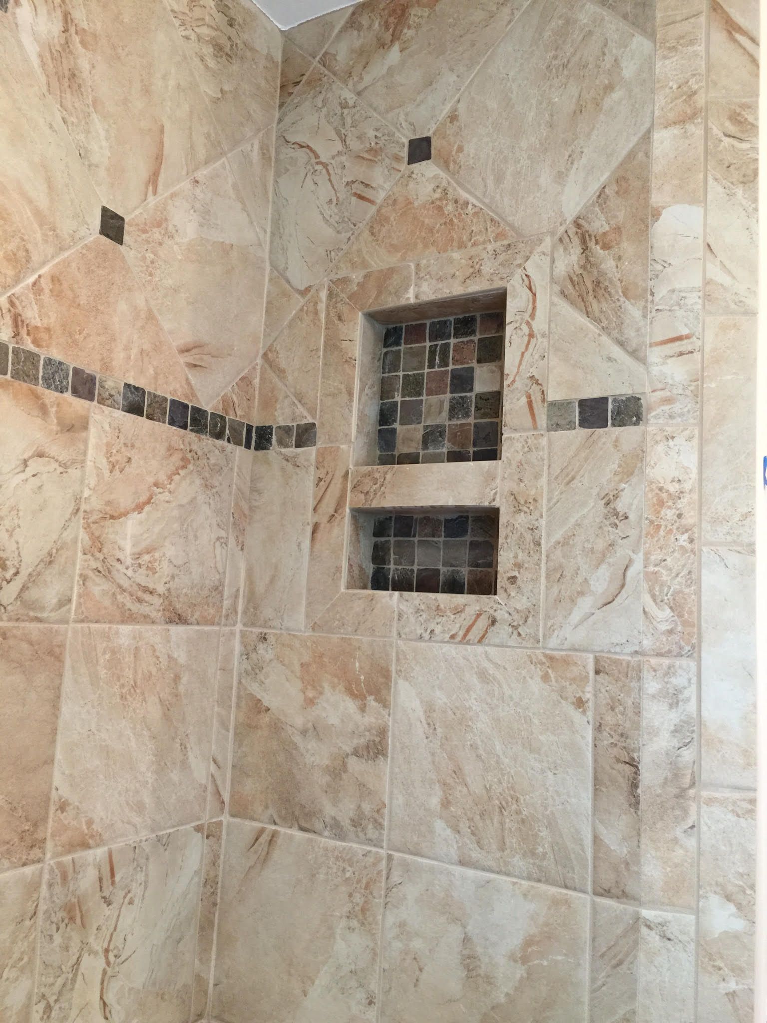 Shower with beige marble tile, mosaic accent in the recessed shelves.