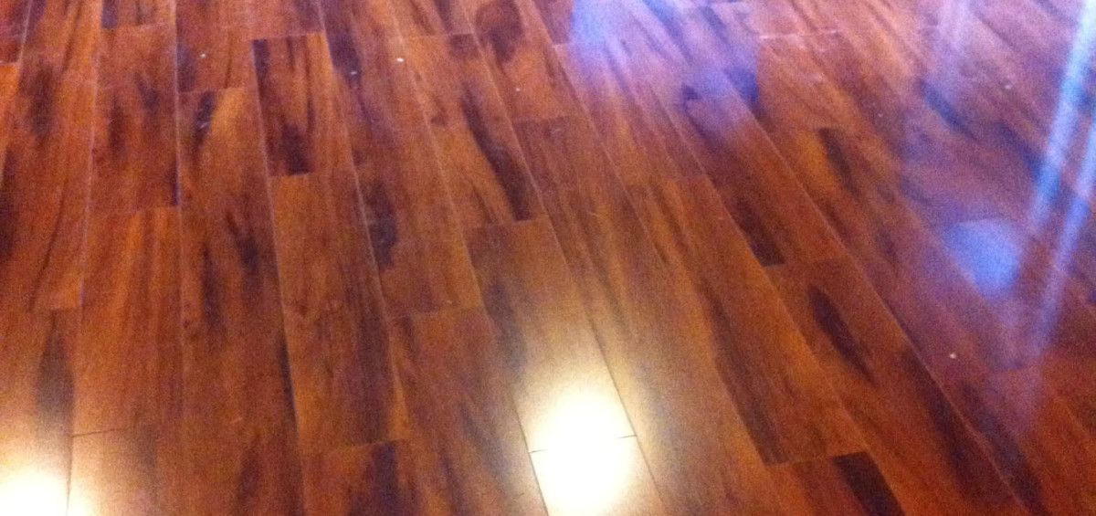 Close-up of a wood floor with a shiny, polished finish. The wood is a warm brown color with darker grains.