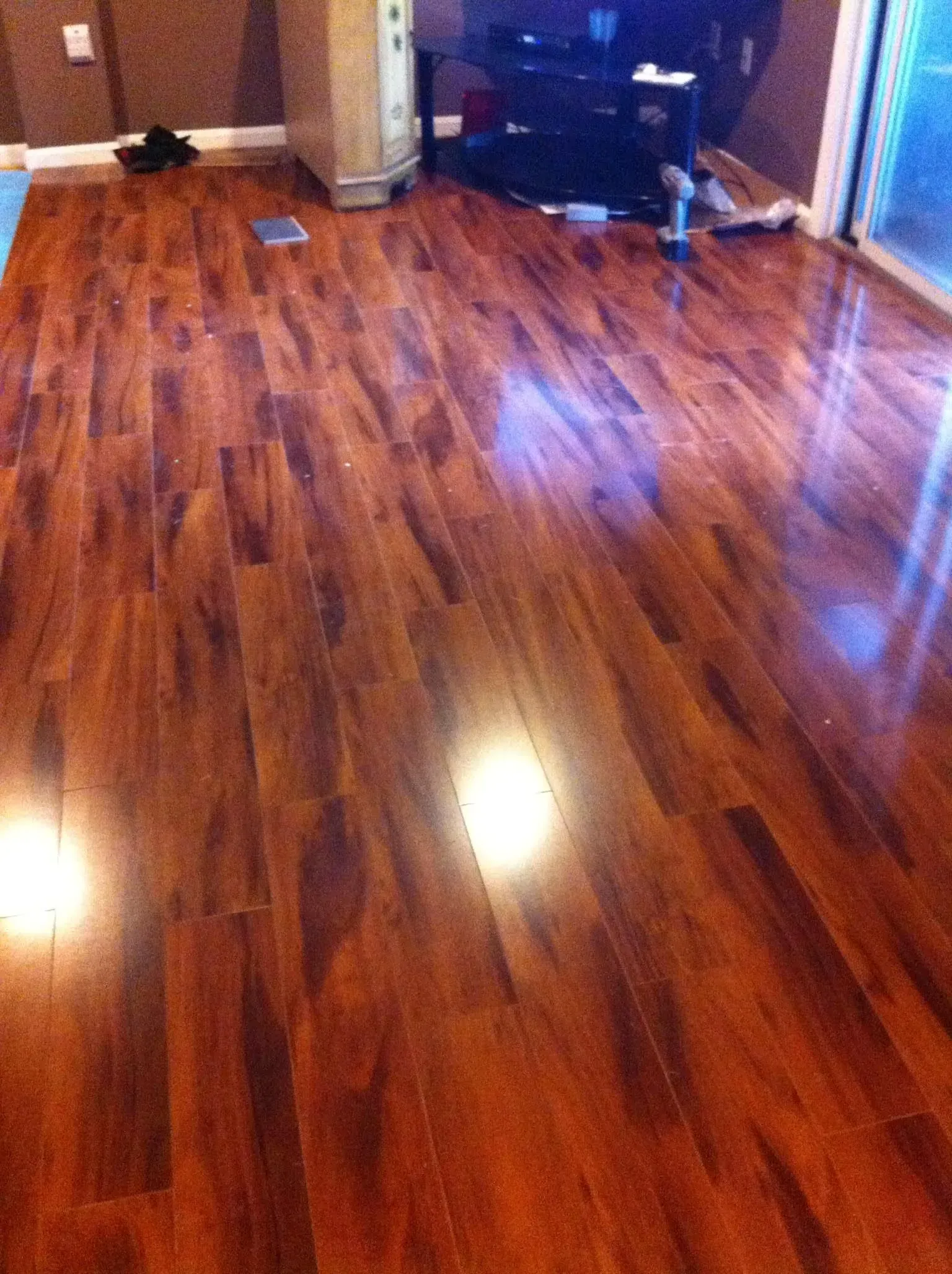 Shiny wood-look laminate flooring in a room, with reflections of light on the surface.