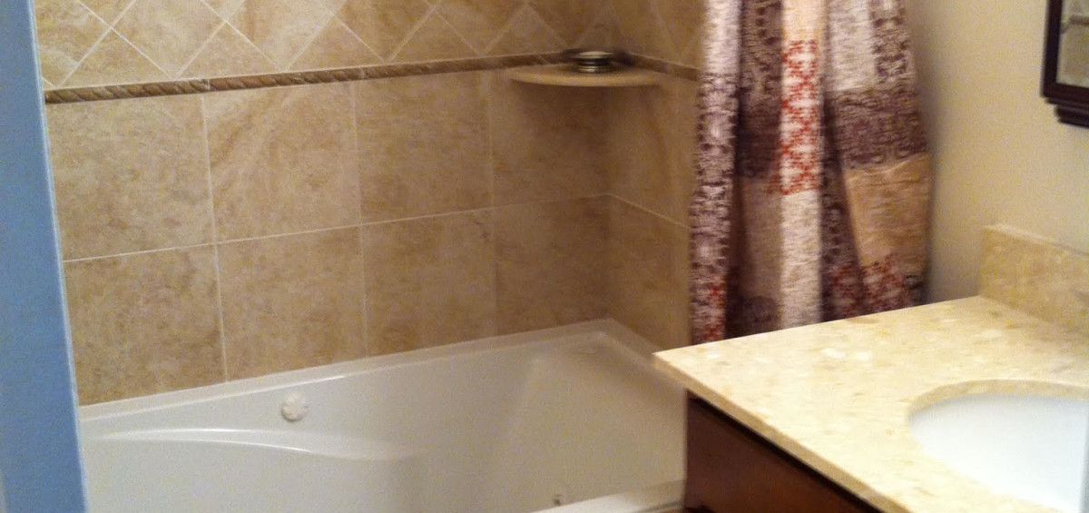 Bathroom with tan tile, a white tub, a brown vanity, and a patterned shower curtain.
