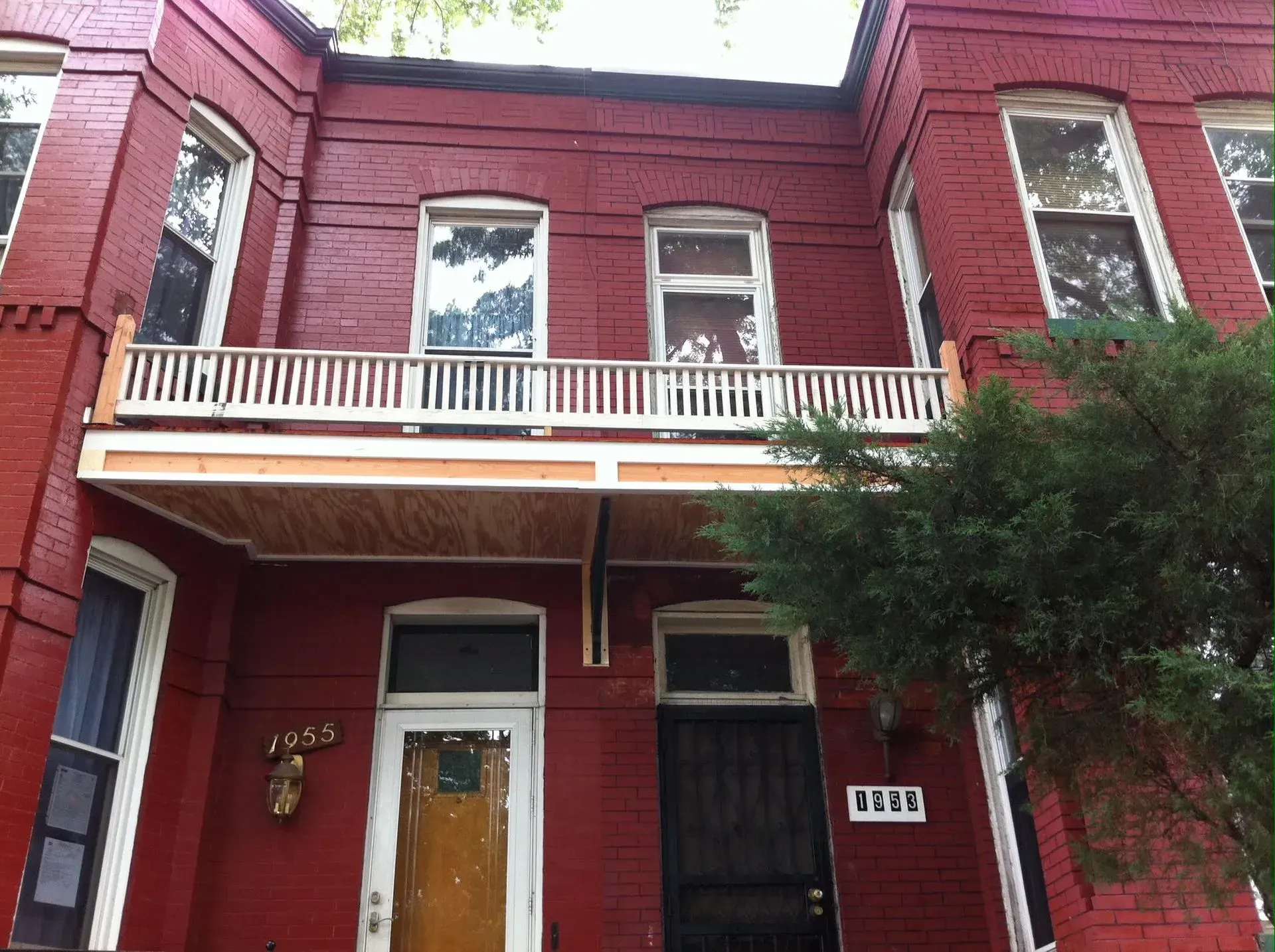 Red brick building with a wooden porch and windows. Doors are visible below the porch.