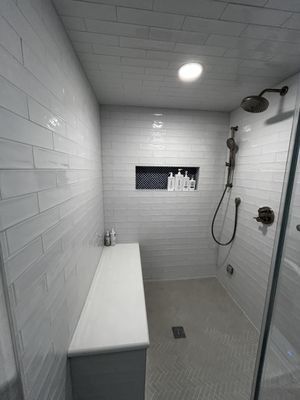 White tiled shower with a built-in bench, dark fixtures, and a shampoo niche.