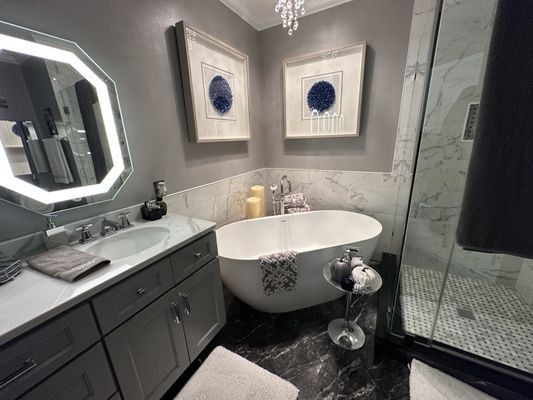 Elegant bathroom with soaking tub, marble accents, gray vanity, and framed art.