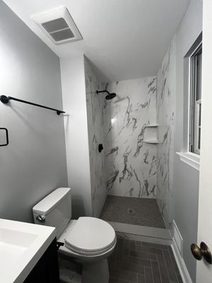 Bathroom with marble-look shower, toilet, sink, dark accents, and gray walls.
