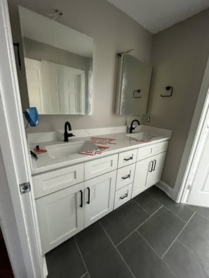 White bathroom vanity with black fixtures, gray countertop, and dark tile floor.