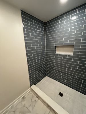 A newly tiled shower with dark blue brick-style tiles, a niche, and a light-colored floor and drain.