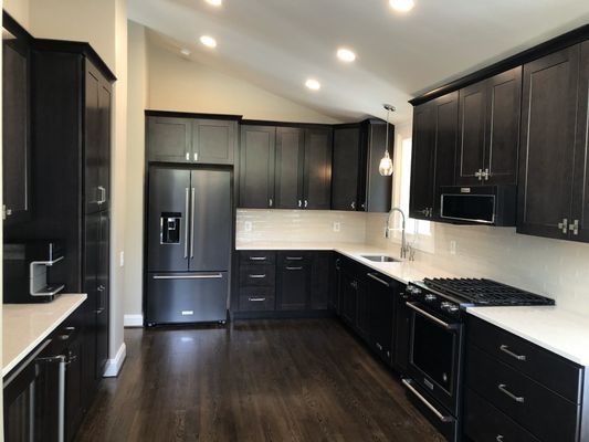 Dark-cabinets kitchen with stainless steel appliances, white countertops, and dark wood floors.