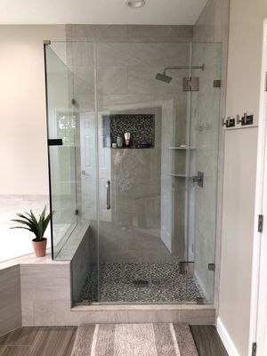 Modern bathroom with a glass shower, gray tiles, and a small pebble floor.