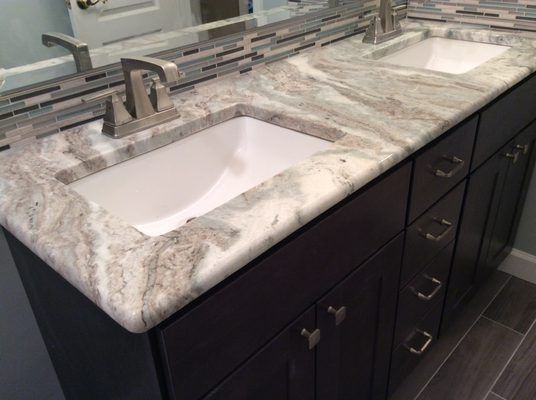 Bathroom vanity with gray marble countertop, two white sinks, and dark brown cabinets.