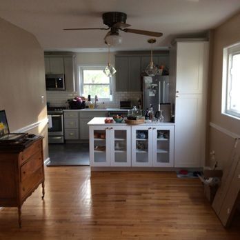 Kitchen with light wood floor, gray and white cabinets, island, stainless steel appliances, and brown ceiling fan.