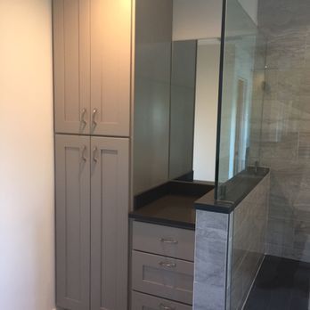 Gray bathroom cabinet with drawers and tall storage next to a glass shower.