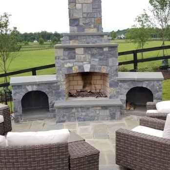 Outdoor stone fireplace with built-in arches, seating area, and field backdrop.