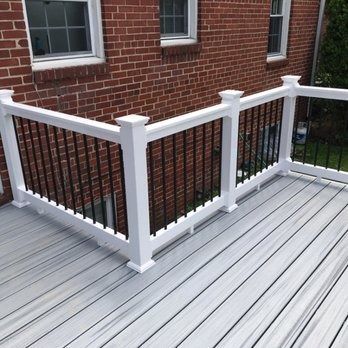 White deck with black railing against a brick building with windows.
