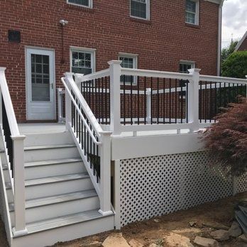 White deck with black railing and steps against a red brick house; lattice skirt.