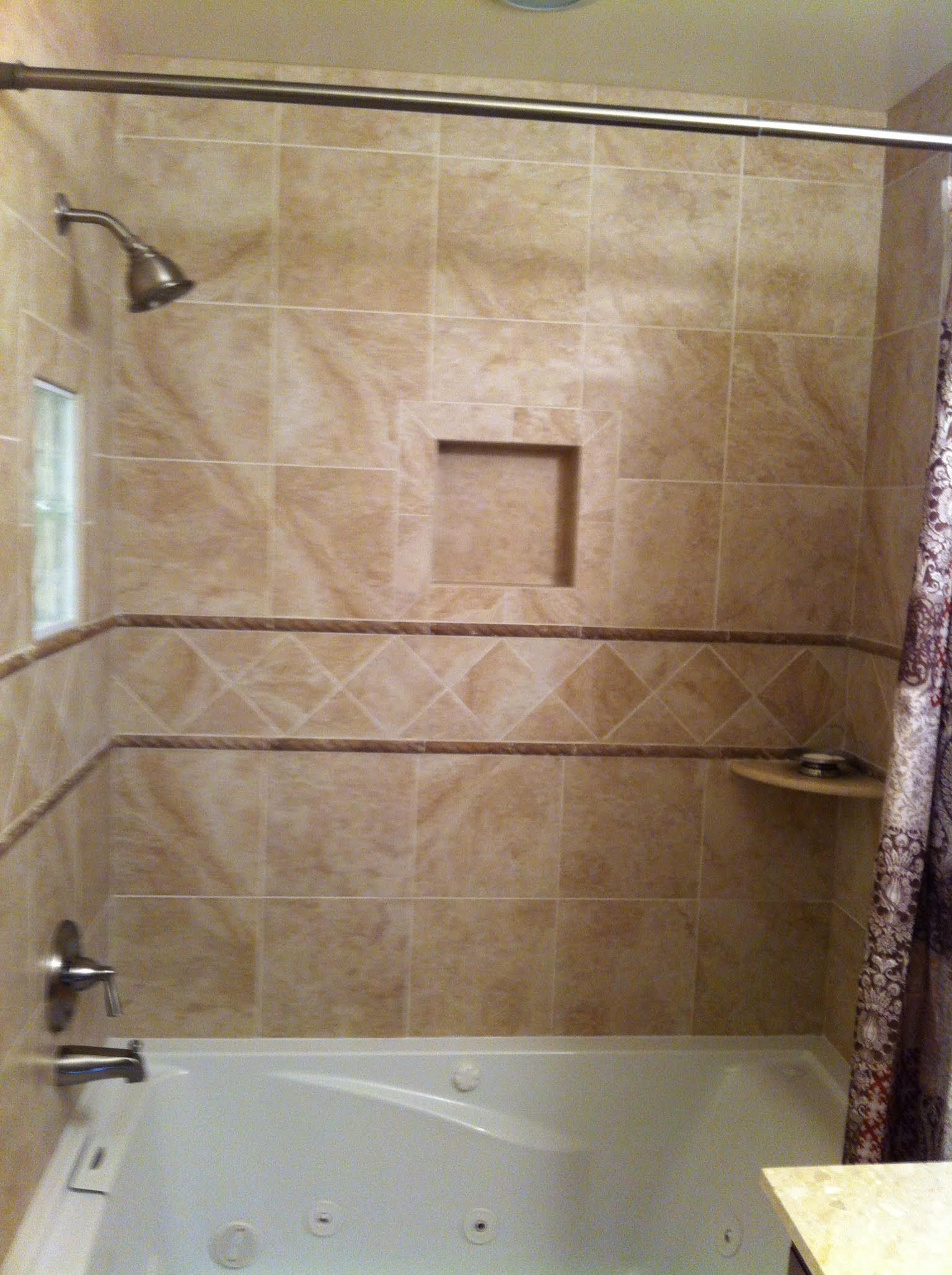 Bathroom with beige tile, showerhead, bathtub, and recessed shelf.