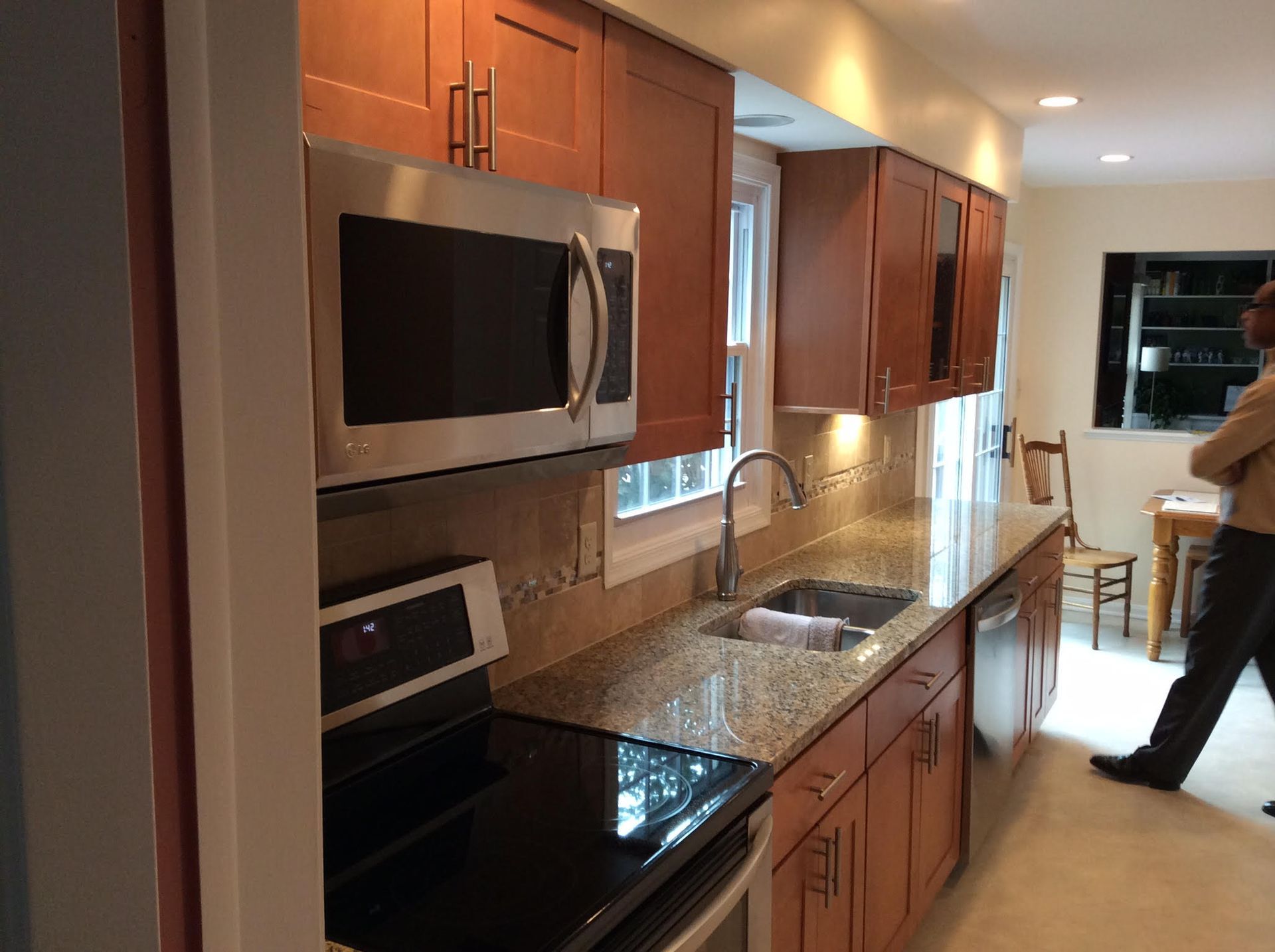 Kitchen with brown cabinets, stainless steel appliances, granite countertops, and a person walking in the background.