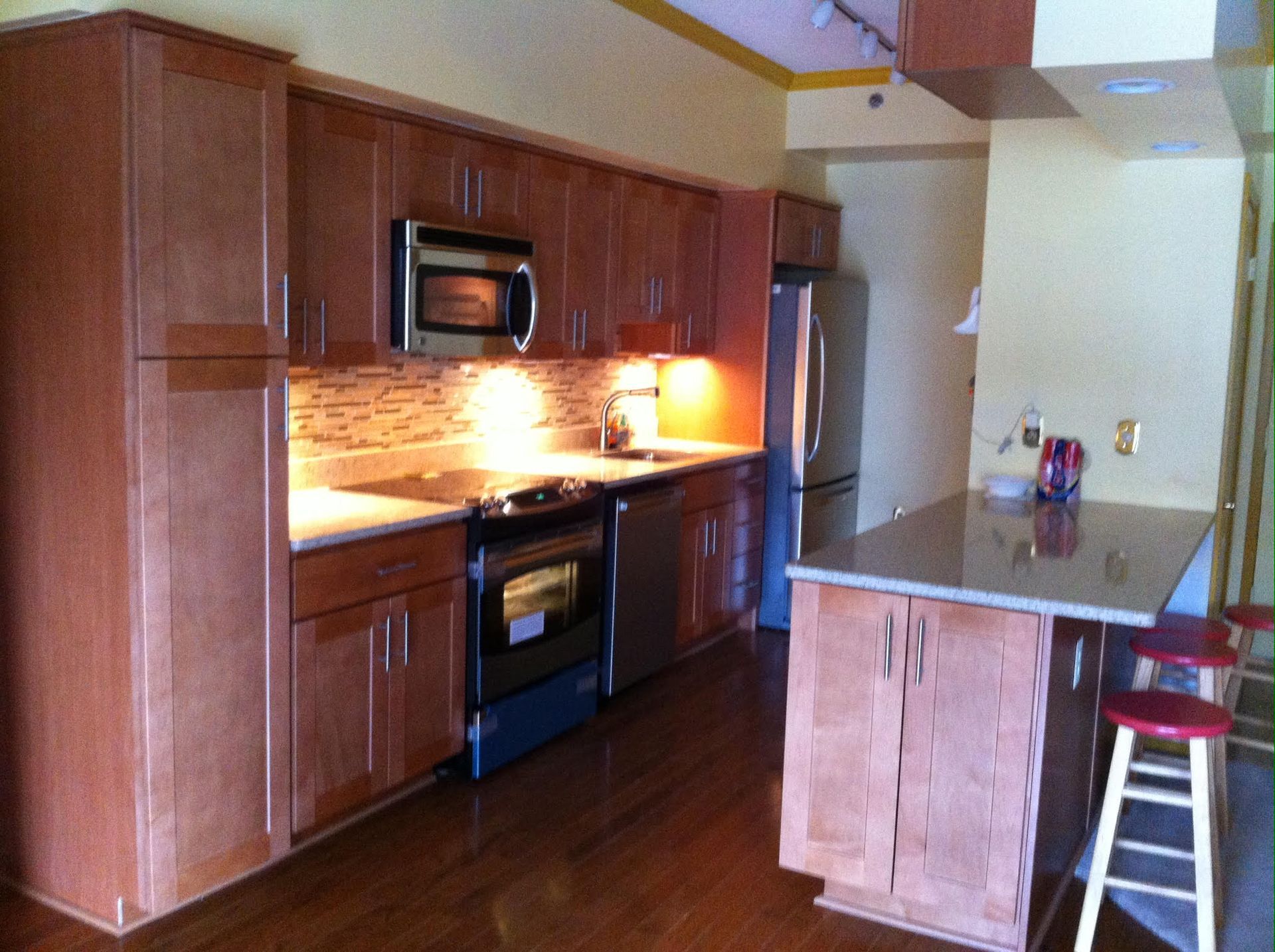 Kitchen with light brown cabinets, stainless steel appliances, a small island, and red bar stool.