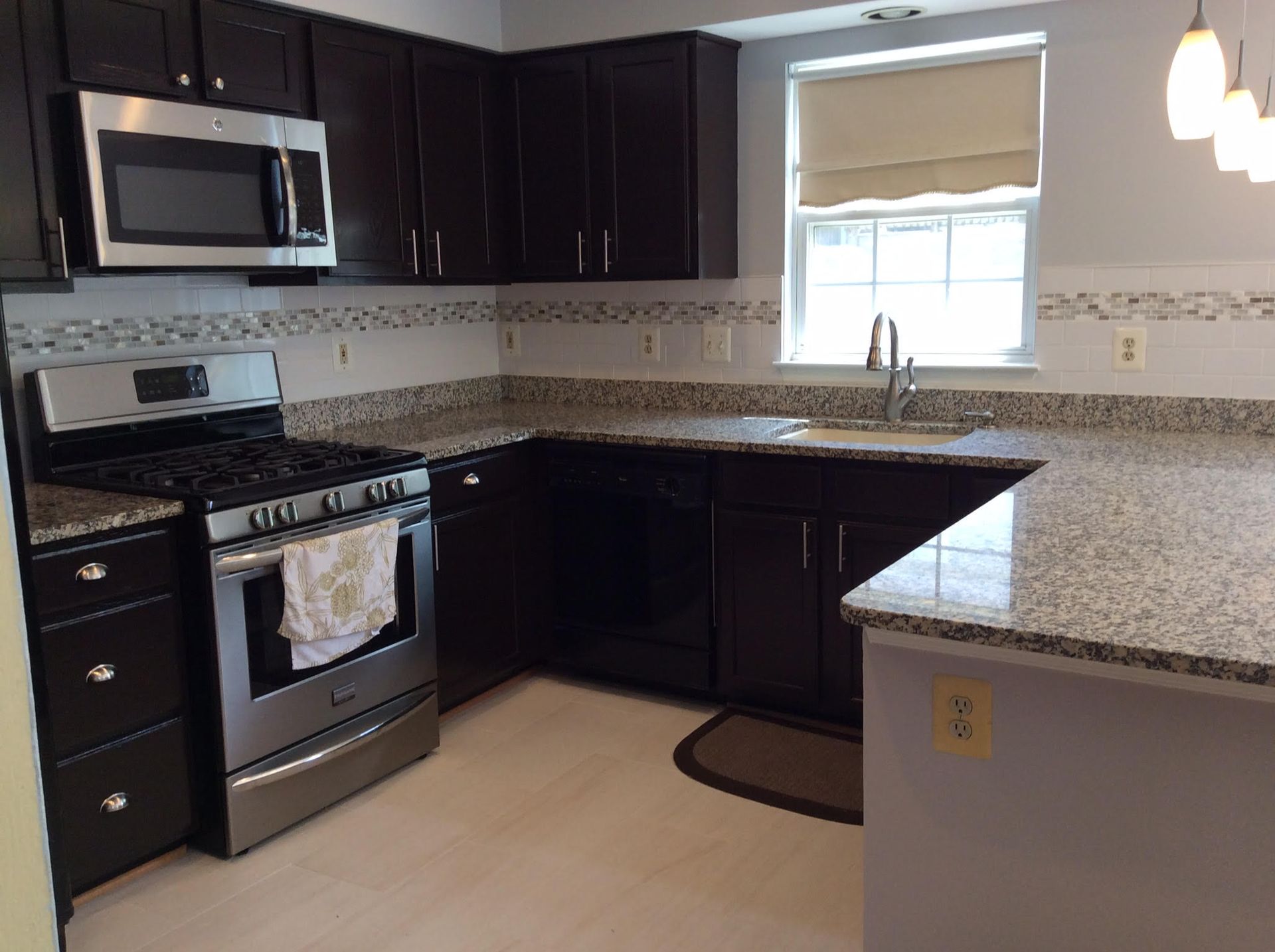 Dark kitchen with granite counters, stainless steel appliances, and a window.