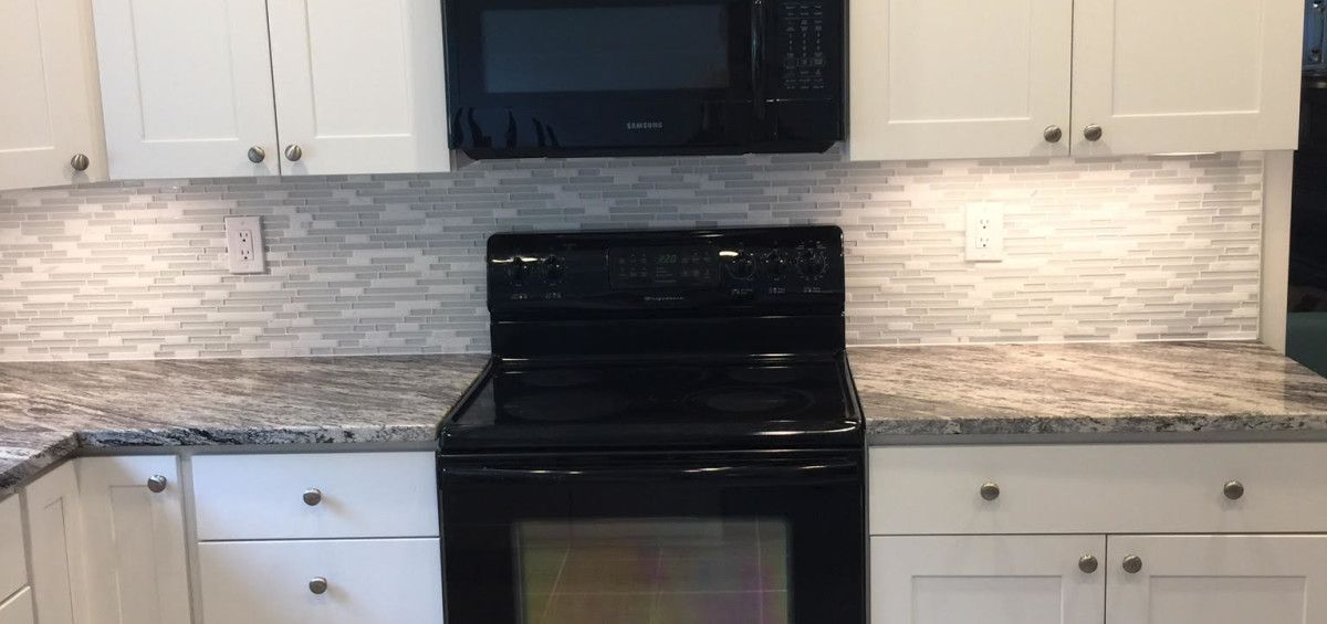 Kitchen with white cabinets, black microwave and stove, and light-colored backsplash.