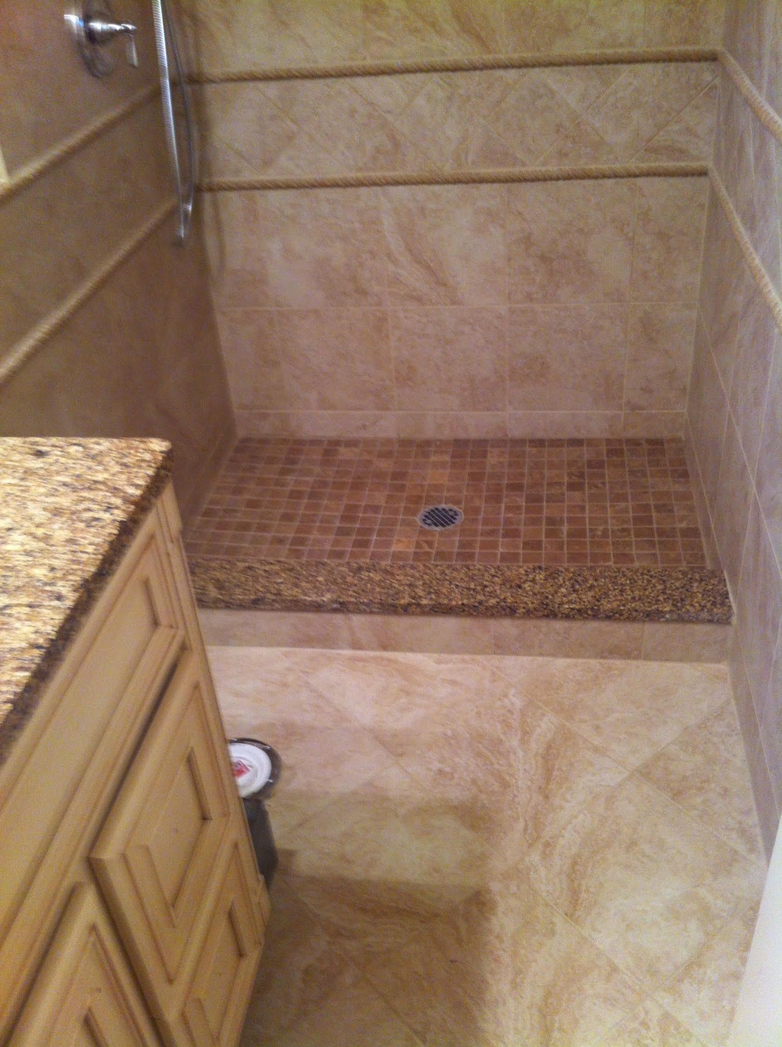 Tiled shower with a pebble floor, tan walls, and a wood vanity in a bathroom.