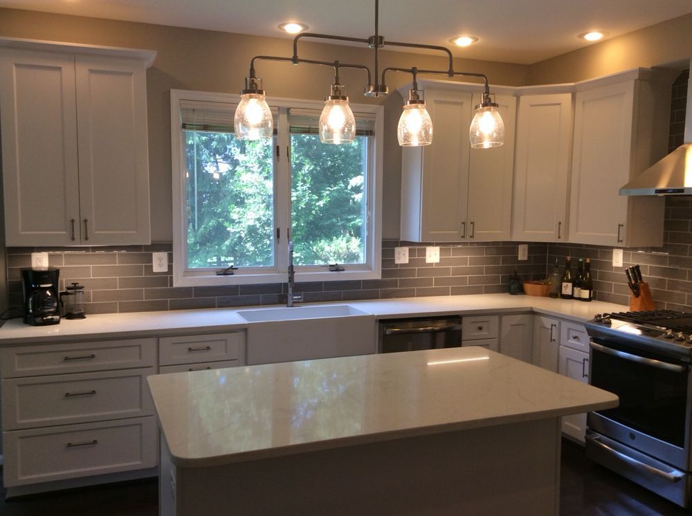 Modern kitchen with white cabinets, gray backsplash, island, and window.