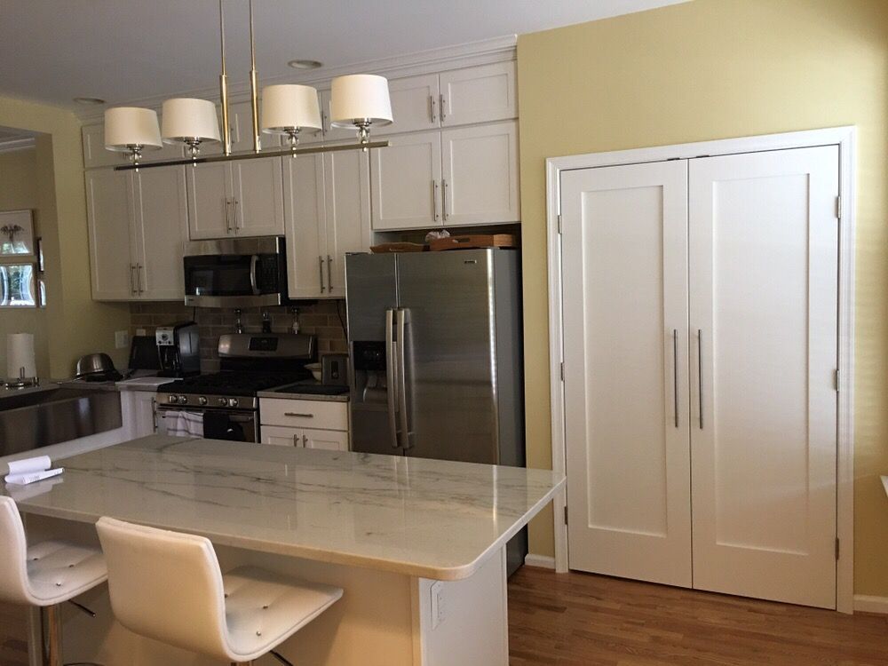 Kitchen with white cabinets, island, and stainless steel appliances. White doors on the right.
