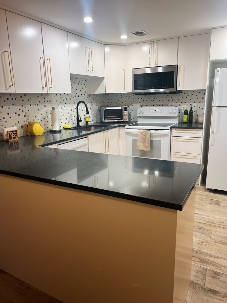 Modern kitchen with white cabinets, black countertops, stainless steel appliances, and a black faucet.