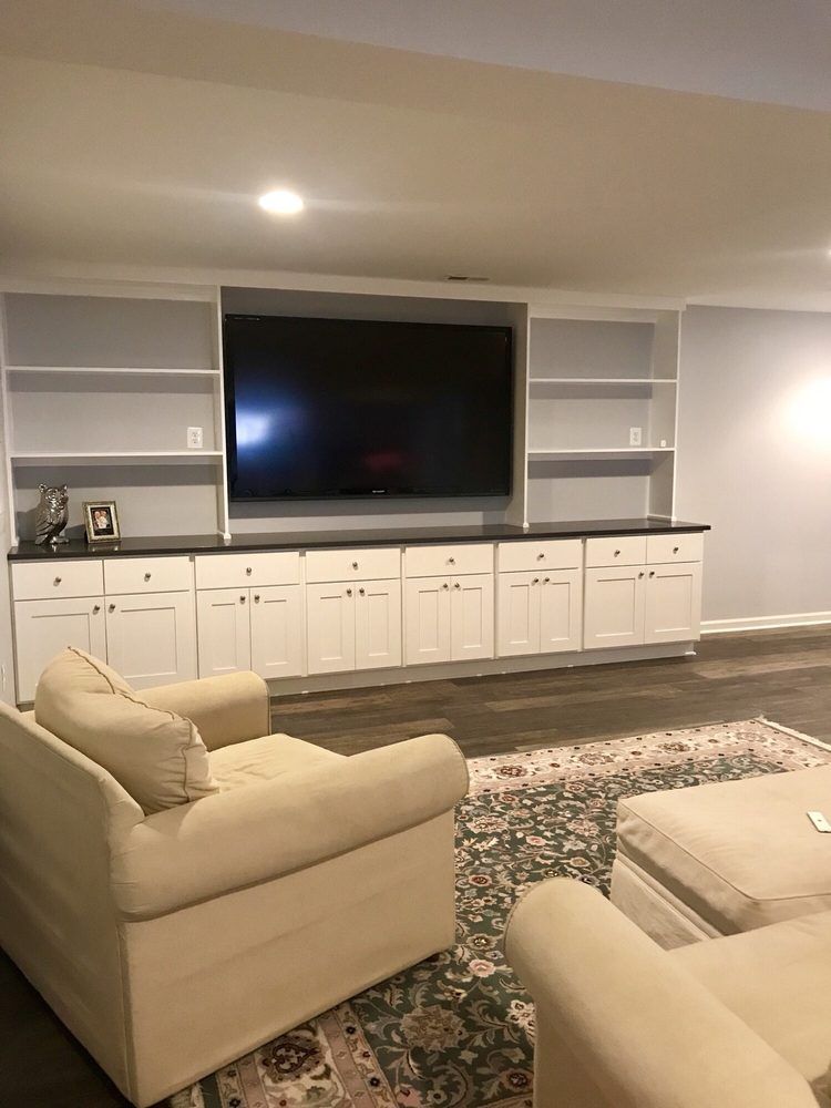 Living room with white built-in cabinets, large TV, beige sofa, and patterned rug.
