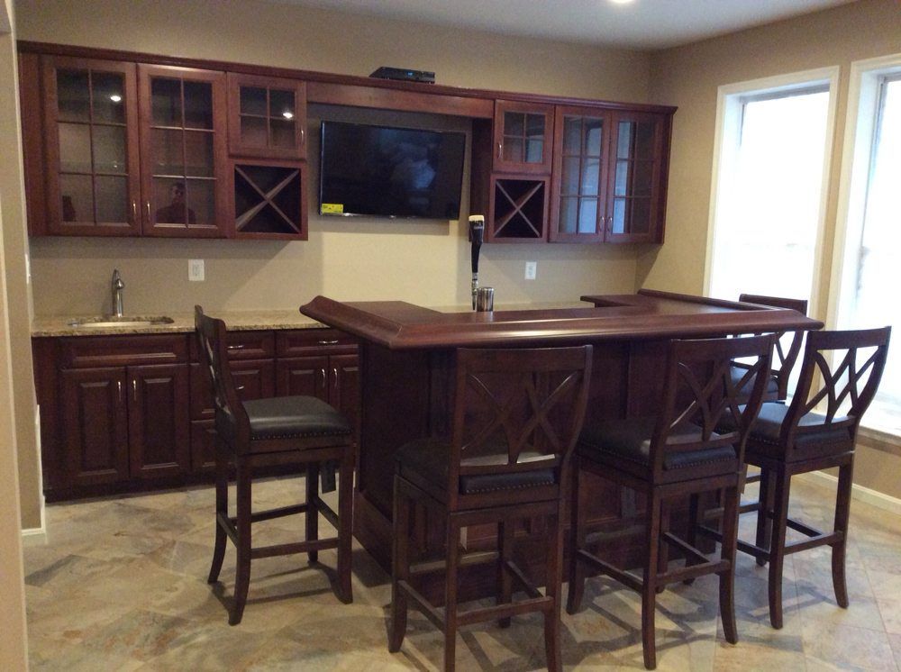A home bar with a dark wood bar and cabinets, stools, a TV, and a sink.