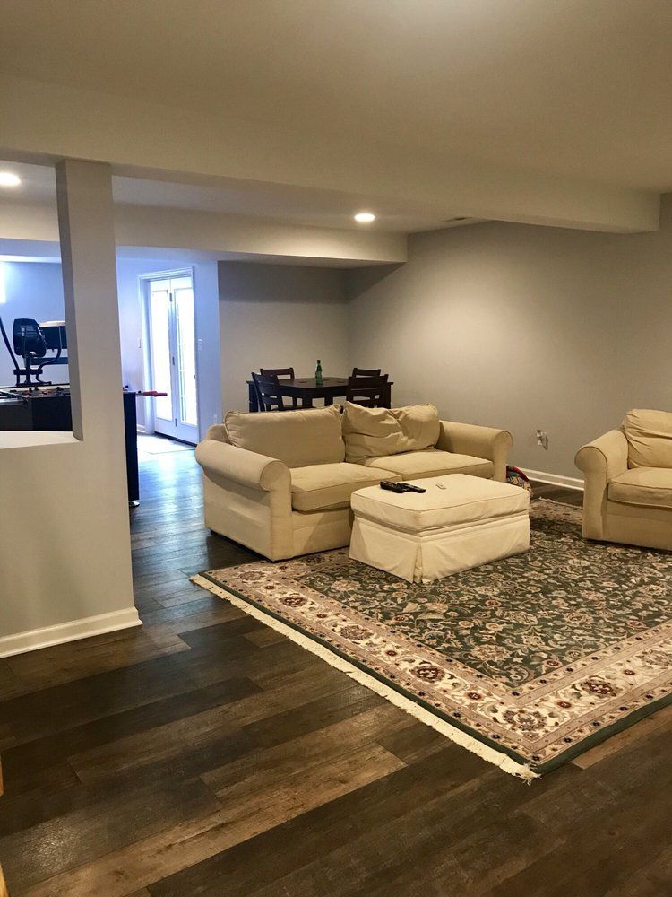 Living room with beige couches, ottoman, and rug on dark wood floor; a dining area in the background.