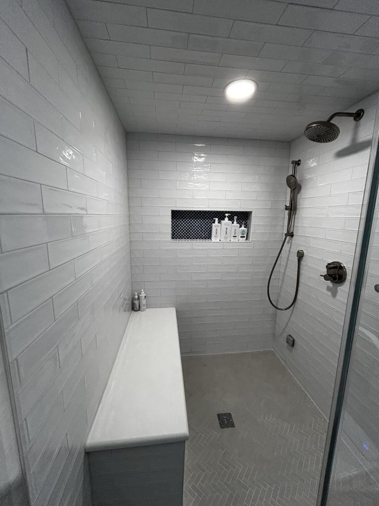 A white tiled walk-in shower with a built-in bench, dark niche, and glass door.