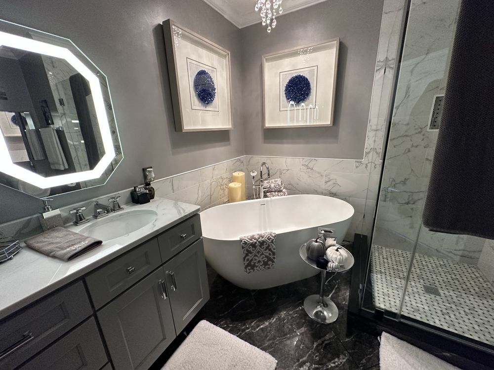 Gray and white luxury bathroom with bathtub, shower, vanity, and artwork.