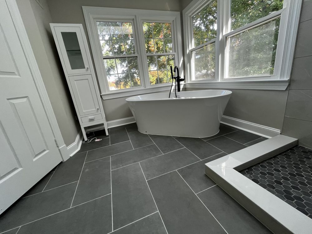Bathroom with freestanding tub, dark tile floor, and large windows.