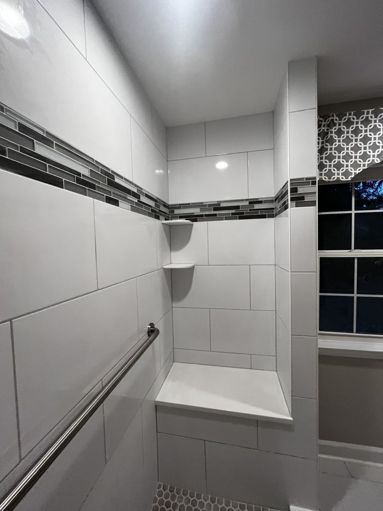 Modern white tiled shower with built-in bench and shelves, accented with a dark glass tile border, and a handrail.