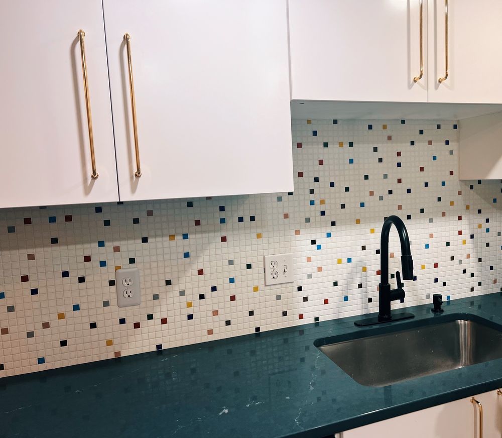 Kitchen with white cabinets, mosaic backsplash, dark countertop, and black faucet.