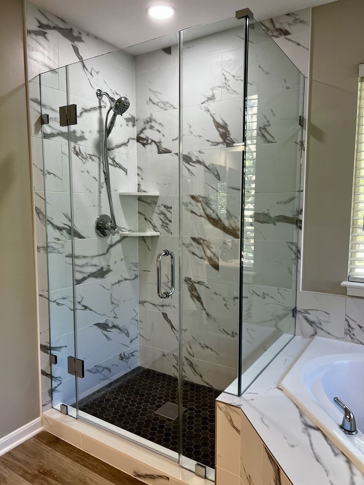 Modern glass shower with marble-look tile, dark floor, and chrome fixtures in a bathroom setting.