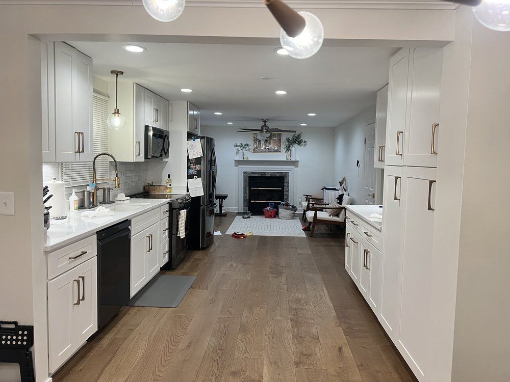 White kitchen with black appliances, leading to living room with fireplace and hardwood floors.