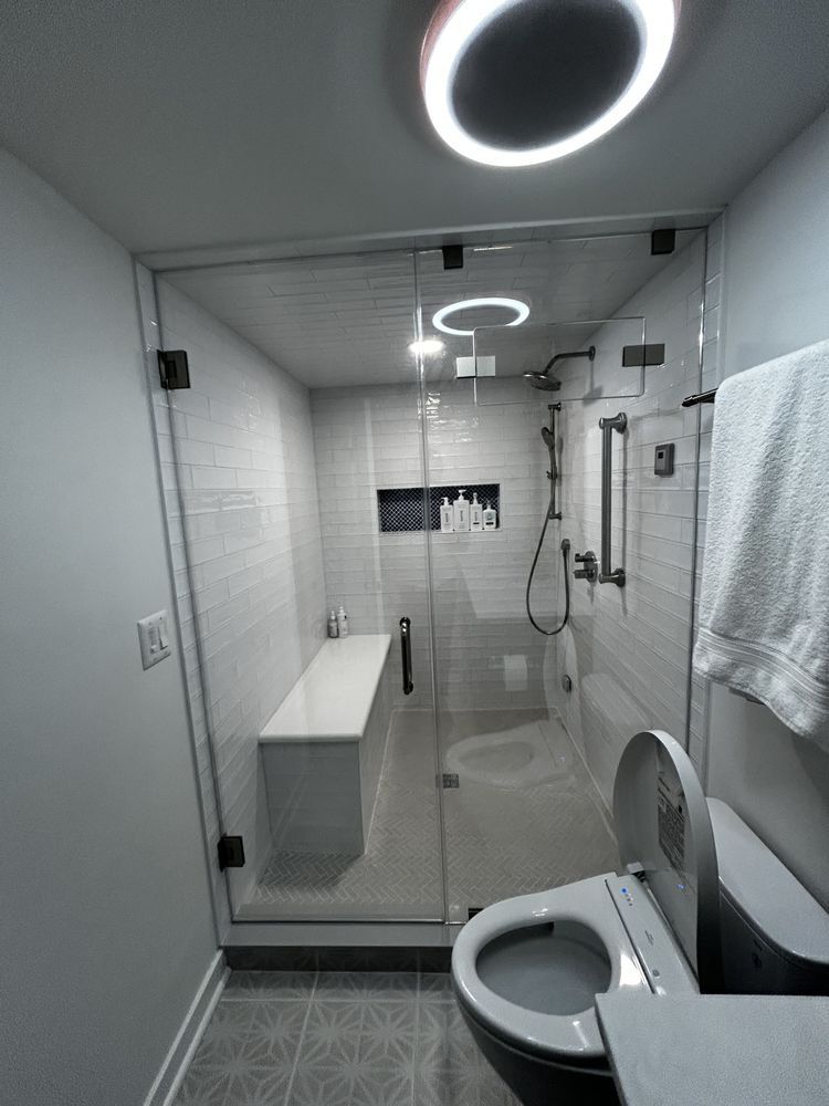 Modern bathroom with glass shower, toilet, white tile, and a bench.
