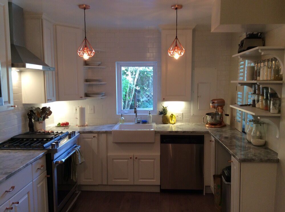 White kitchen with copper pendant lights, stainless steel appliances, and window.