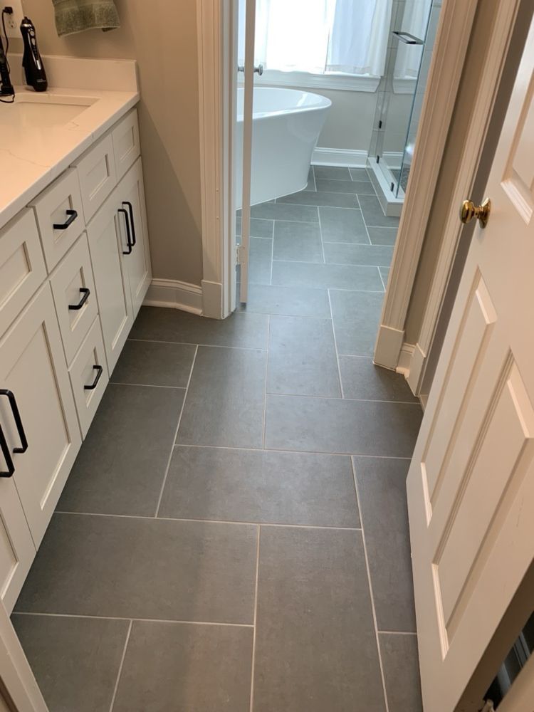 Gray tiled bathroom floor leading to a bathtub and shower. White vanity on the left.