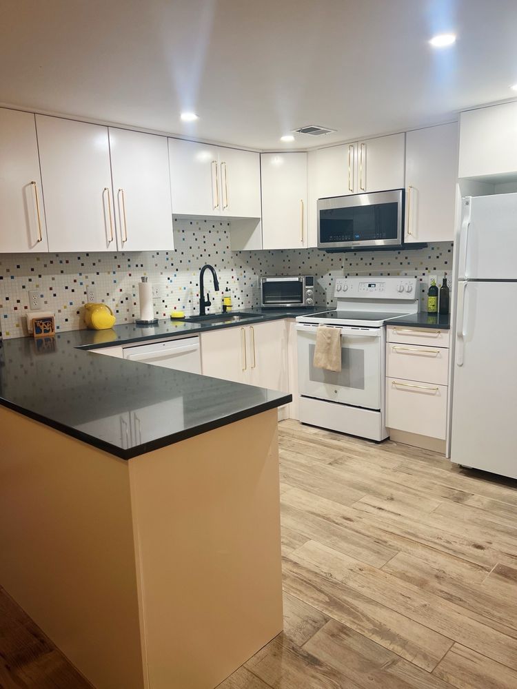 U-shaped kitchen with white cabinets, black countertops, and wood-look flooring. Includes appliances and a yellow accent.