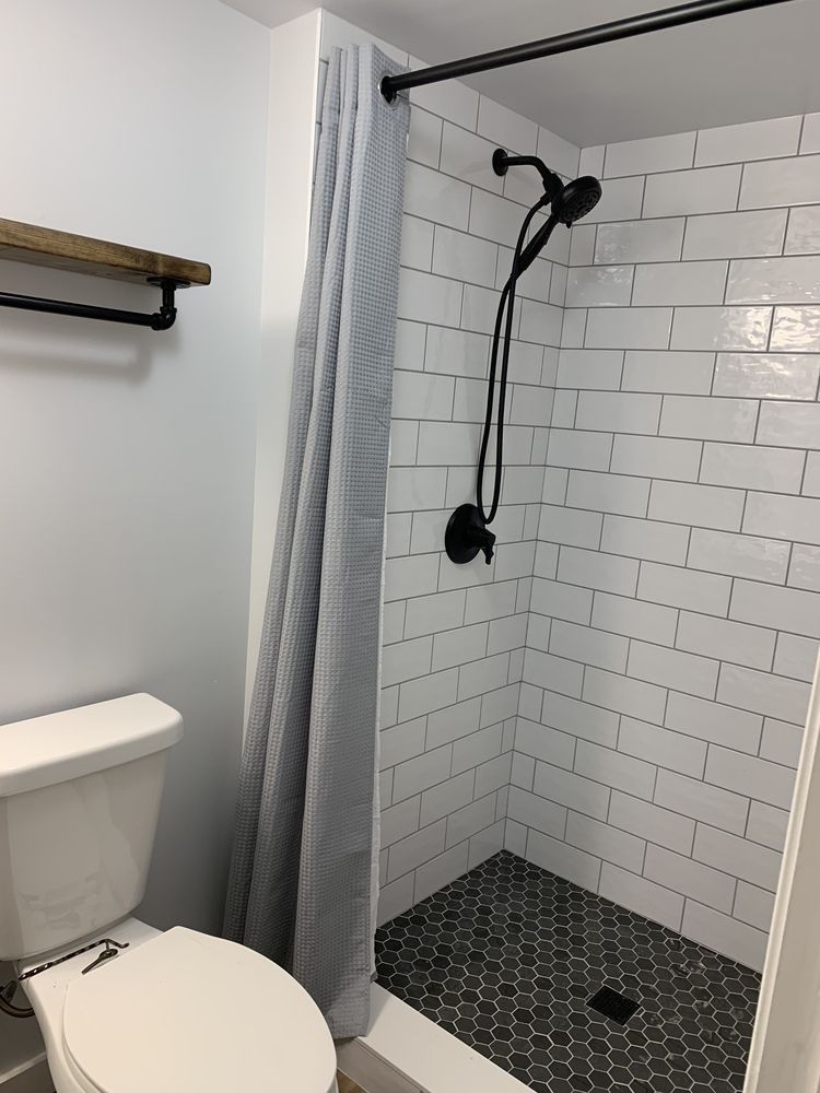 Small bathroom with white subway tile shower, black fixtures, and toilet. Gray shower curtain.