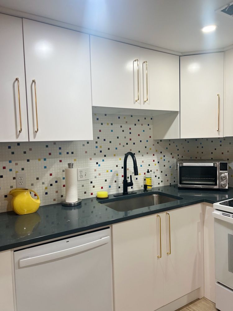White kitchen with dark countertops, black sink, and colorful mosaic backsplash.
