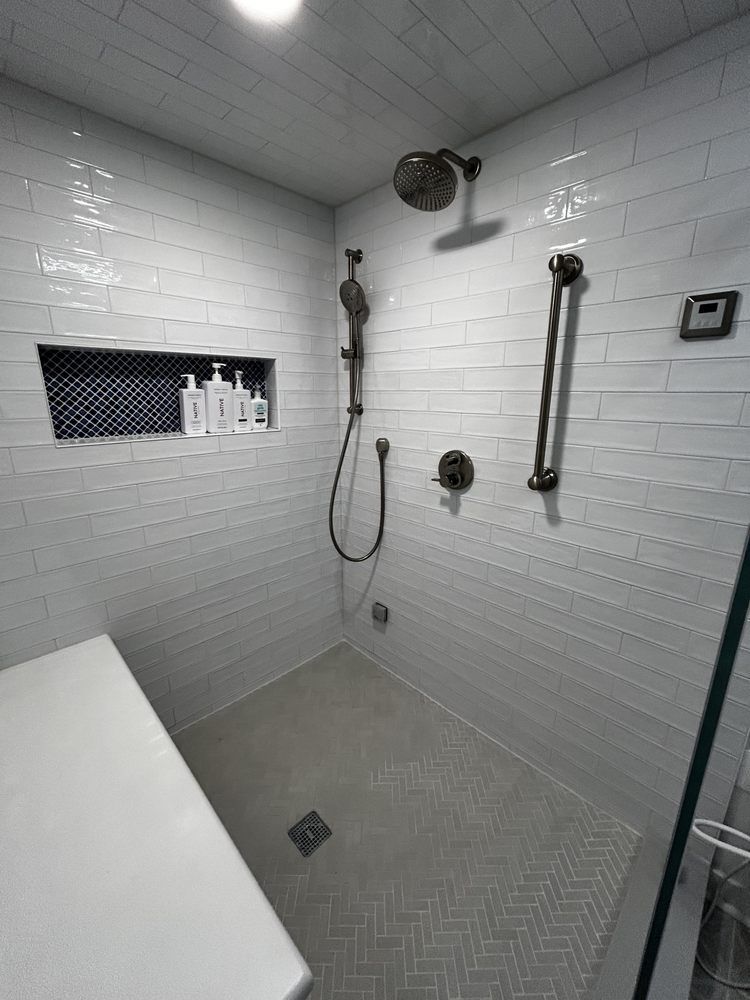 Modern white tiled shower with a bench, gray floor, and shower fixtures.