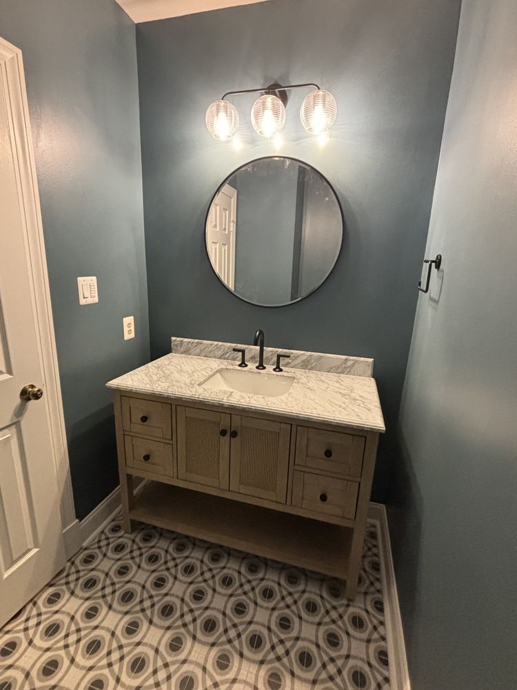 Powder room with blue walls, patterned floor, wood vanity, round mirror, and globe light fixture.