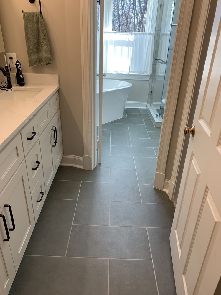 Bathroom with gray tile floor, white vanity and door, and bathtub near window.