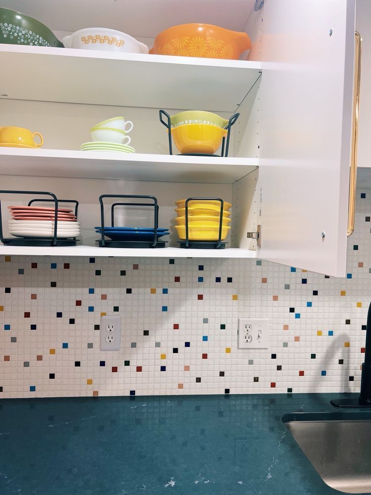 Kitchen cabinet with colorful dishes and mosaic backsplash.